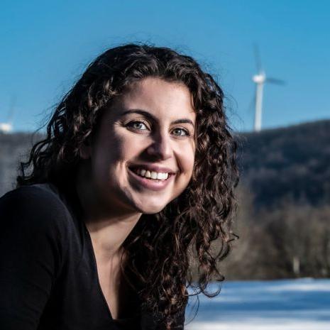 Andrea Poosikian smiles in front of three wind turbines standing in the distance.